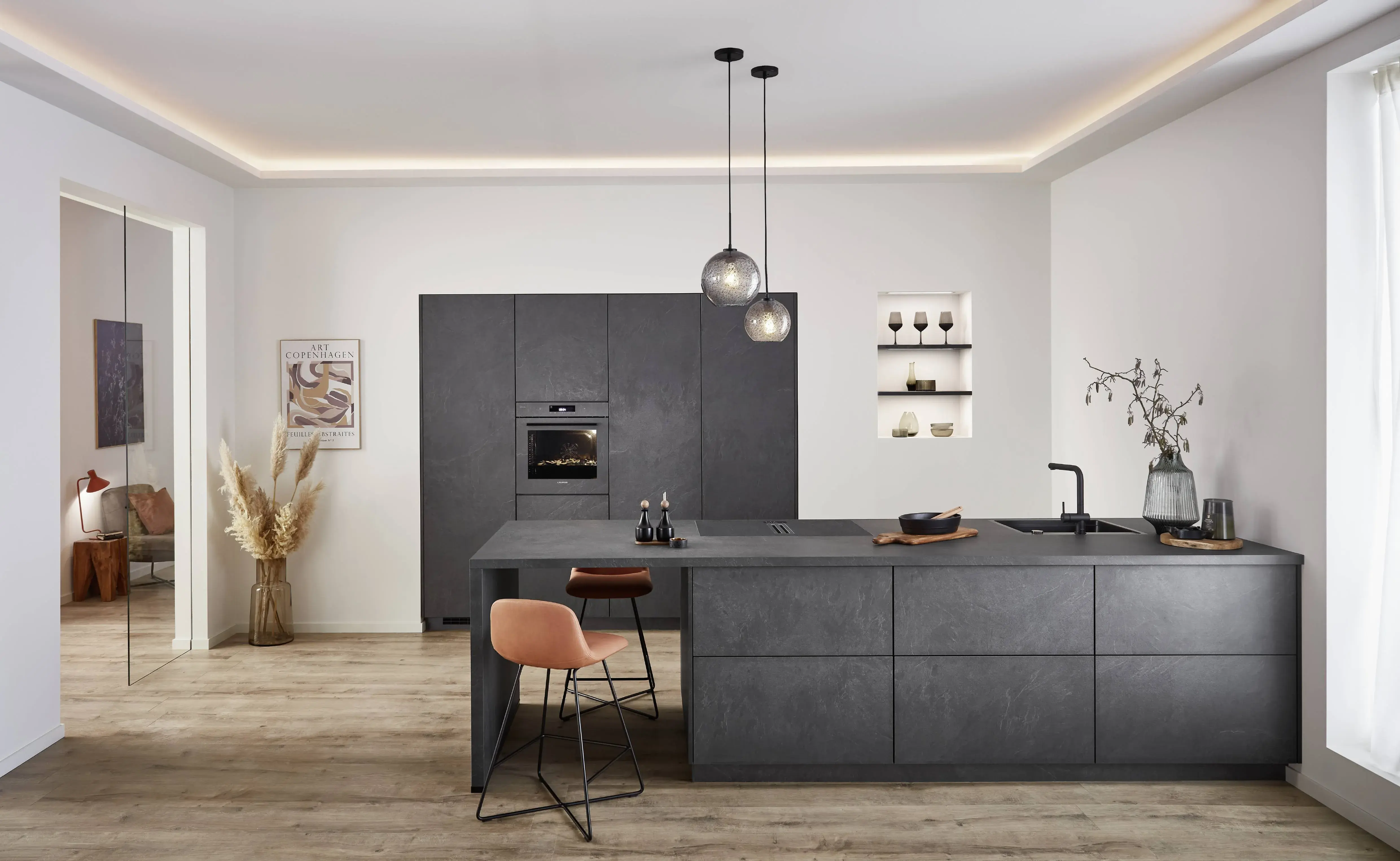 Nobilia Stoneart dunkelgraue Inselküche mit Thekenansatz davor cognacfarbene Barstühle auf filigranen Metallfüßen